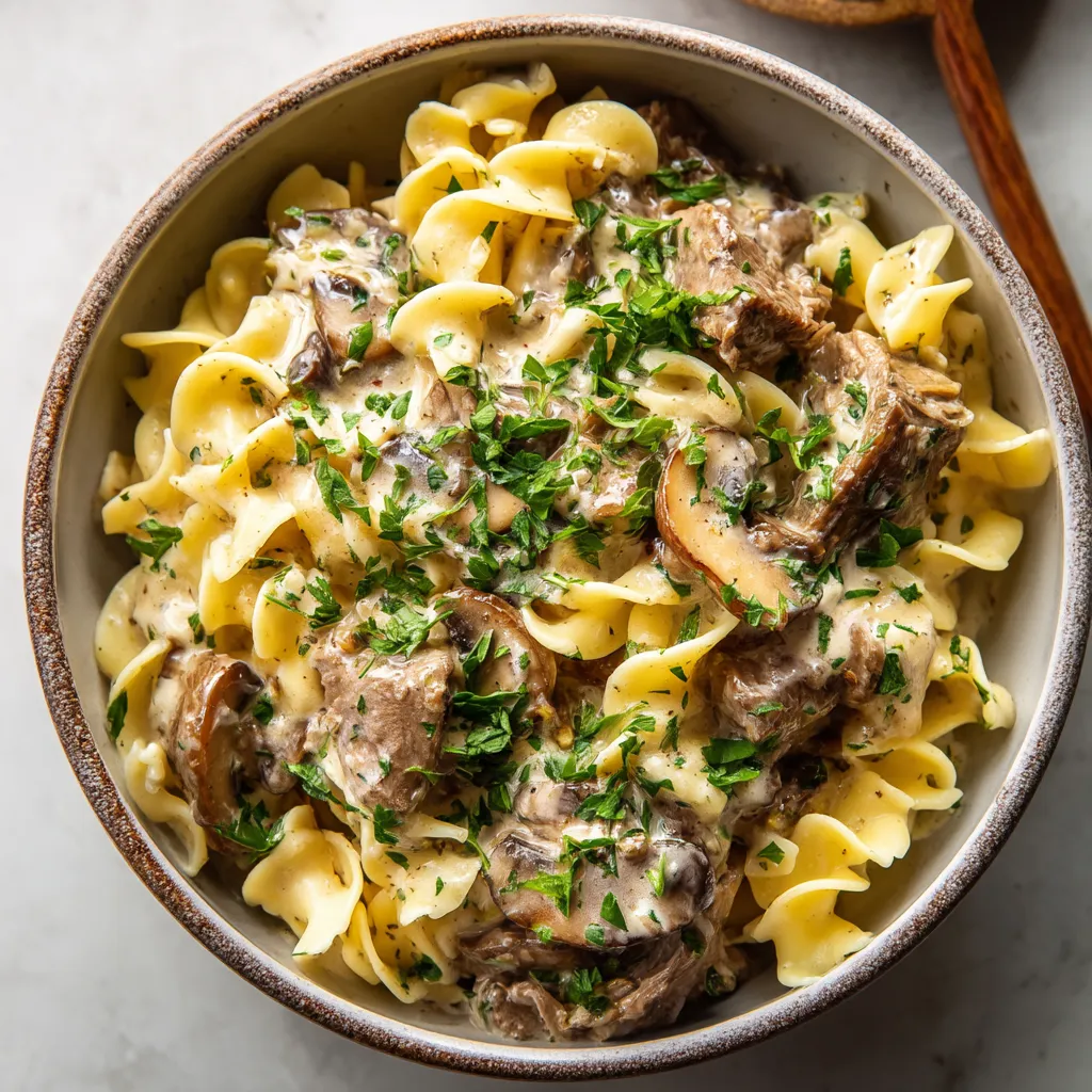 A bowl of pasta with meat and mushrooms.