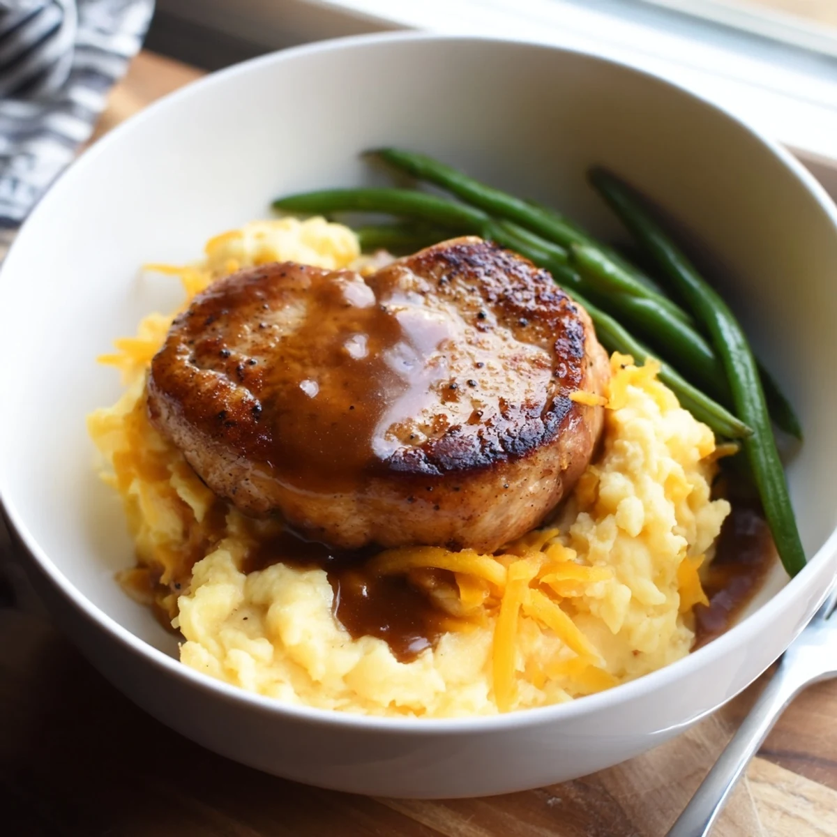 Sizzling pork chops topped with rich pan gravy over velvety cheddar mash delight.