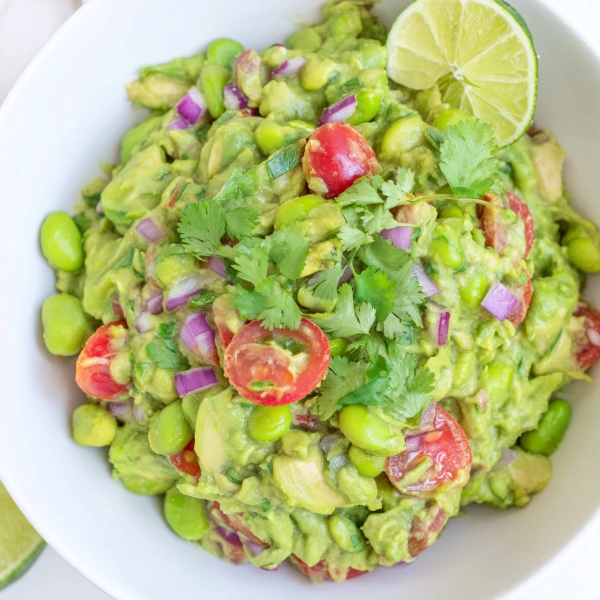 Creamy, green Edamame Guacamole, sprinkled with red onion, cilantro, and served with a lime wedge.