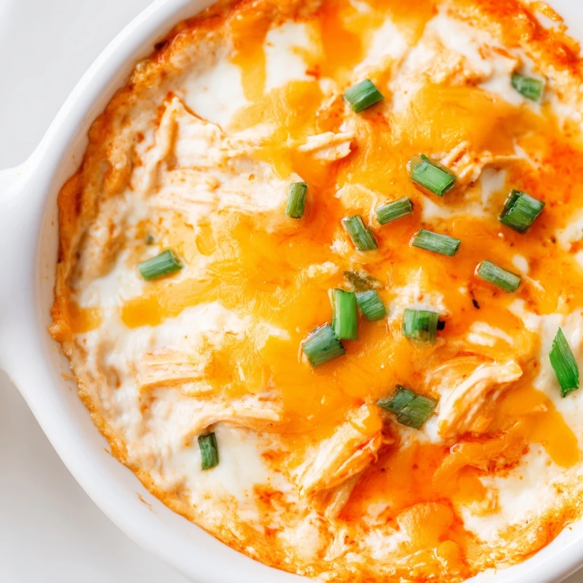 A golden, baked version of Crock Pot Buffalo Chicken Dip in a serving dish, garnished with extra cheese and served with tortilla chips.