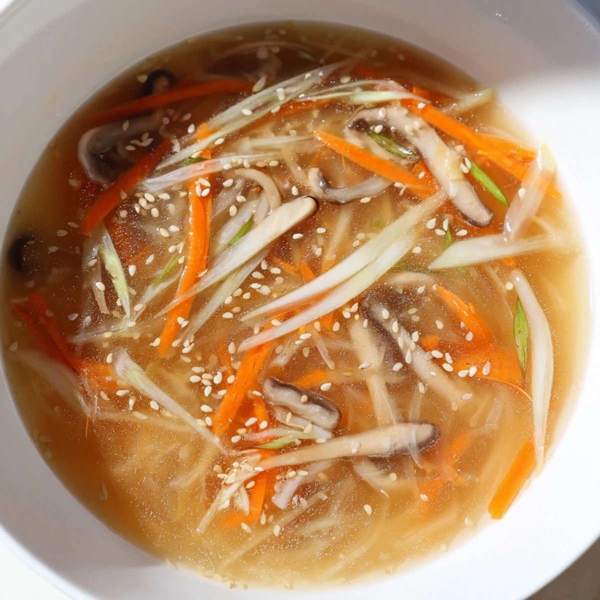 A close-up bowl of Ginger-Miso Winter Soup features tender shiitake mushrooms, julienned carrots, and napa cabbage in a warm, umami-rich broth garnished with scallions.