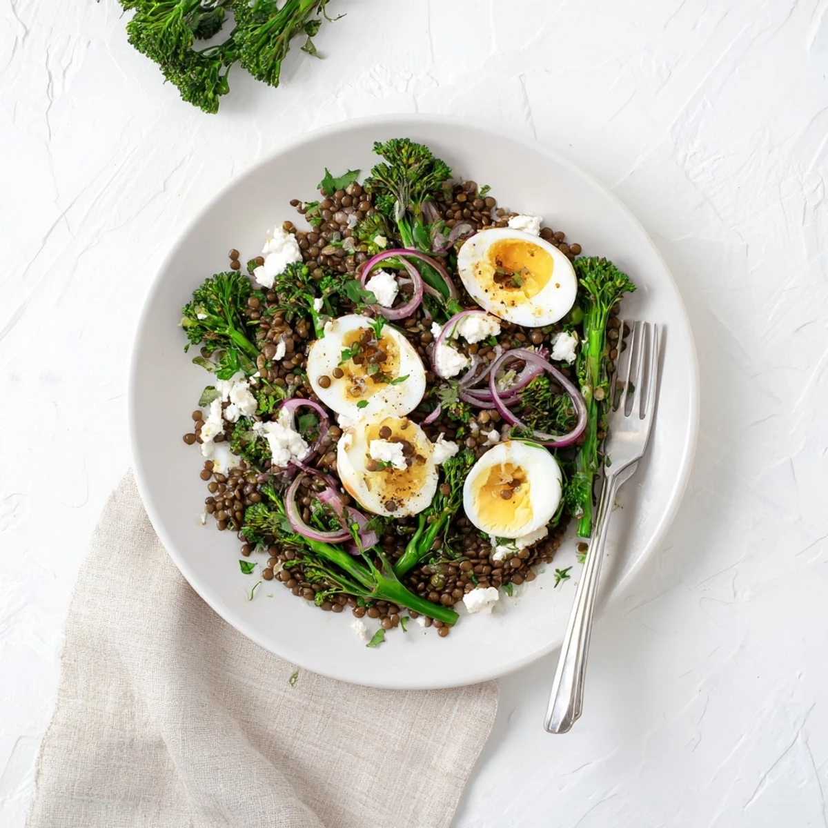 Hearty vegetarian French lentil salad with blanched broccolini, red onion, and halved soft-cooked eggs.