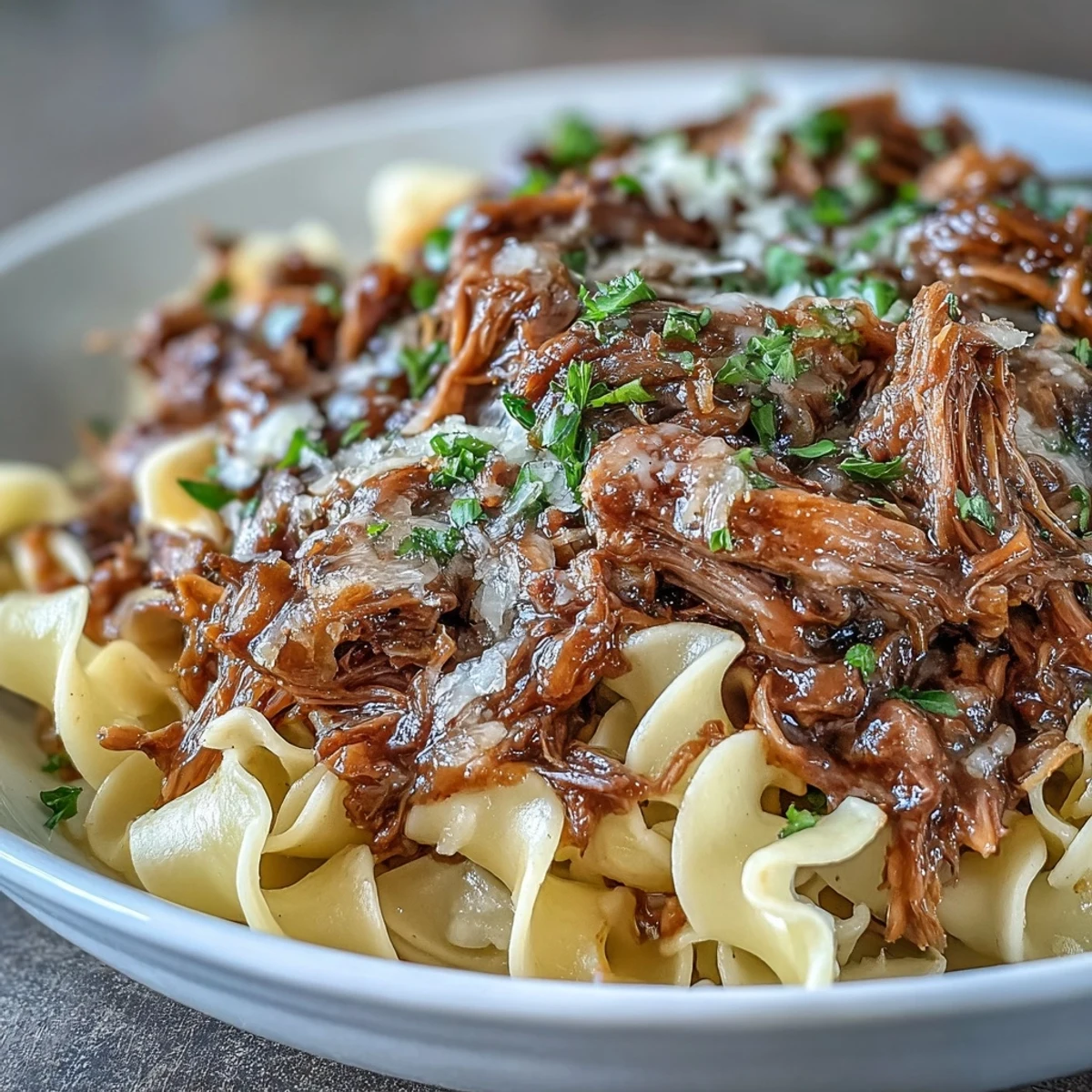 Shredded Crockpot French Onion Pot Roast Pasta served over buttery egg noodles, with rich onion gravy.