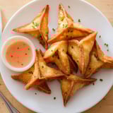 Savory Crispy Pumpkin Wonton Bites recipe: Triangle-shaped, stuffed dumplings, served with a red dipping sauce.