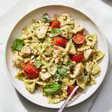 Delicious bowl of pesto chicken bowtie pasta garnished with pine nuts and tomatoes.  