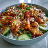 A close-up of a vibrant Bang Bang Chicken Bowl with fluffy rice, juicy chicken, crunchy veggies, and a drizzle of creamy, spicy sauce.