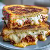 Golden-brown Sun-Dried Tomato Pesto Grilled Cheese oozing melted mozzarella on a plate.