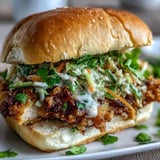 Golden-brown Thai fried chicken sandwich on a toasted brioche bun, layered with pickled carrots and fresh cilantro.  