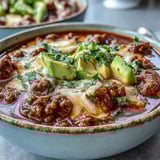 A bowl of Keto Taco Soup with Ground Beef, Cheese, and Avocado, showing creamy texture, melted cheddar, and lime wedges for zest.