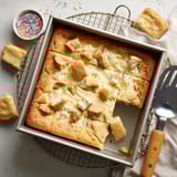 A slice of cake with white frosting and sprinkles.