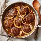A pan of meat with onions and gravy.