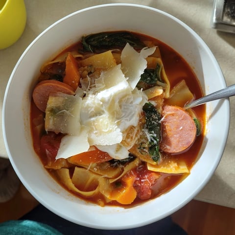 Close-up bowl of Lasagne Soup with Smoked Sausage, showing rich red broth and toppings.