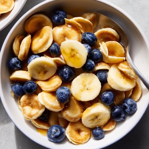 Mini Pancake Cereal served in a bowl with fresh berries and syrup drizzling over.  