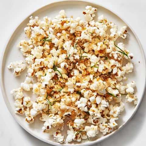 Golden, buttery savoury popcorn mix speckled with herbs and spices, ideal for a shareable snack board.