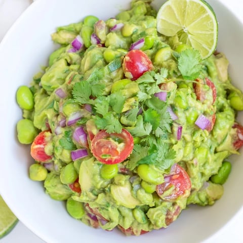 Creamy, green Edamame Guacamole, sprinkled with red onion, cilantro, and served with a lime wedge.