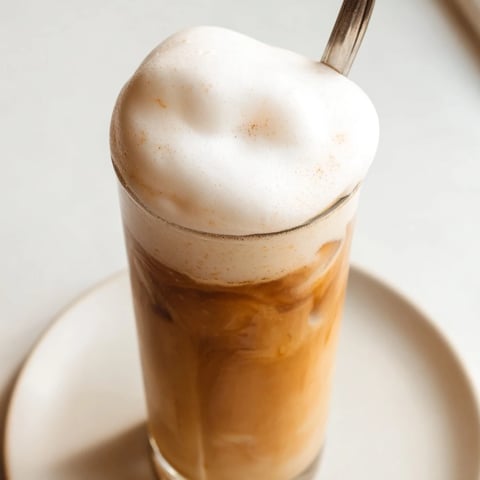 Fluffy Starbucks Cold Foam rests atop a chilled iced coffee, beautifully swirled in a clear glass.