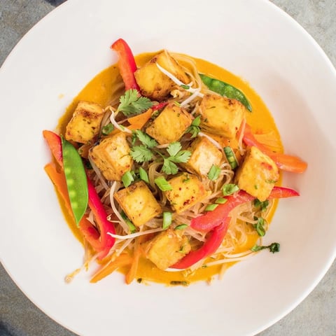 Steaming bowl of Malaysian Laksa Curry, featuring vibrant noodles, vegetables, and creamy broth.