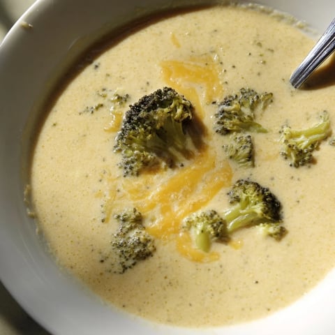 Steaming bowl of creamy Broccoli Cheddar Soup, garnished with vibrant green broccoli florets.
