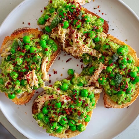Golden toasted bread crowned with creamy Smashed Pea & Chicken Toast, sprinkled with chili flakes and fresh herbs.