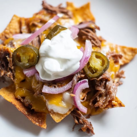 Golden melted cheese blankets smoky barbecue beef nachos, piled high with crisp tortilla chips and colorful fresh toppings.