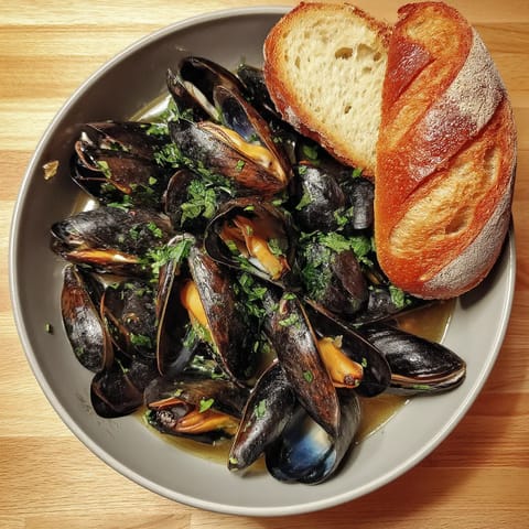 A bowl of mussels with a slice of bread.
