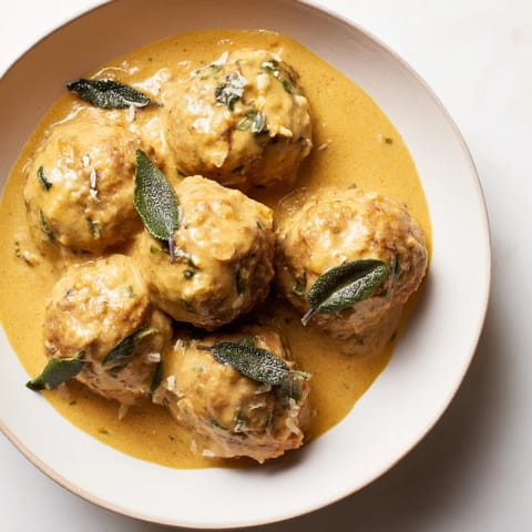 A close-up of a bowl overflowing with savory turkey meatballs and vibrant pumpkin sage sauce.