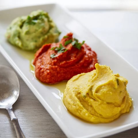 A colorful Dip Trio: three vibrant dips, creamy avocado, roasted pepper, and golden hummus, ready to be enjoyed.