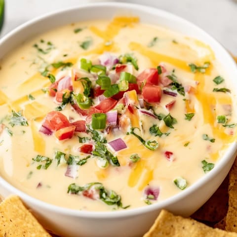 Steam rises from a smooth, spicy Queso Dip made with sharp cheddar and Monterey Jack, garnished with jalapeños and red onion for a flavorful Tex-Mex appetizer.