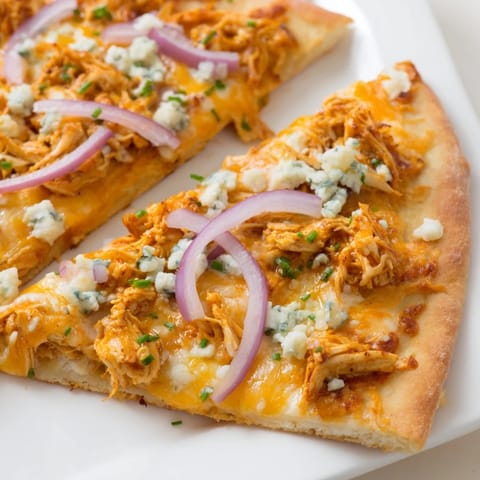 Sliced wedge of Buffalo Chicken Pizza showing spicy chicken, red onion, and blue cheese crumbles on a crispy crust for game day.