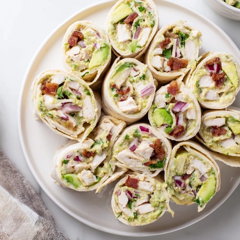 Colorful avocado chicken bacon pinwheels rolled tightly and served with dipping sauce.