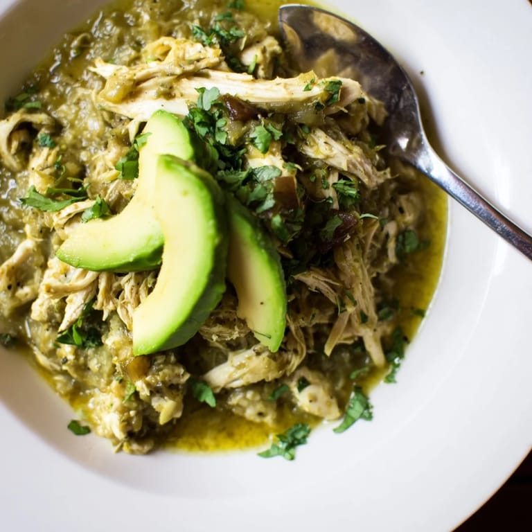 A steaming bowl of Chicken Chili Verde served with lime wedges and warm tortillas, perfect for a cozy dinner.