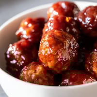 Sticky grape jelly and chili sauce meatballs glisten in a slow cooker, ready for a party appetizer platter.